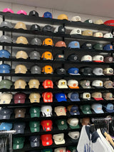 A vibrant collection of baseball caps displayed on black shelves, featuring a variety of colors and team logos.